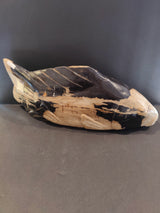 Sculpture shaped like a fish carved from petrified wood displaying contrasting natural beige and black colors with textured patterns.