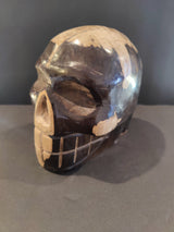Polished skull sculpture carved from petrified wood, showing a blend of dark brown and light beige tones with visible texture contrasts and natural patterns.