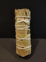 Small bundle of sage leaves tightly wrapped with white string and decorated with tiny dried flower petals against a black background.
