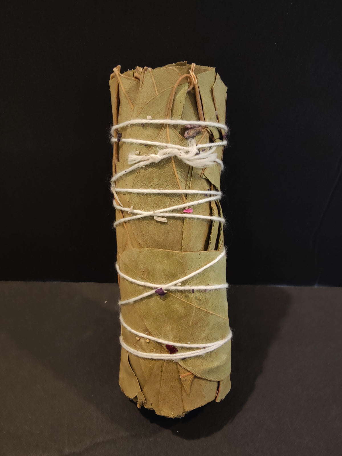 Small bundle of sage leaves tightly wrapped with white string and decorated with tiny dried flower petals against a black background.