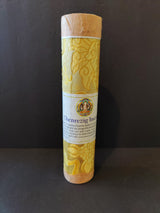 Tall cylindrical bundle wrapped in yellow fabric with floral patterns, topped and bottomed with brown paper caps, featuring a white label with Tibetan artwork and text.