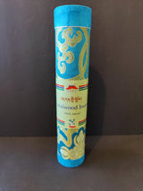 Tall cylindrical container with blue and gold ornate swirling patterns labeled 'Sandalwood Incense 100% natural' against a plain dark background.