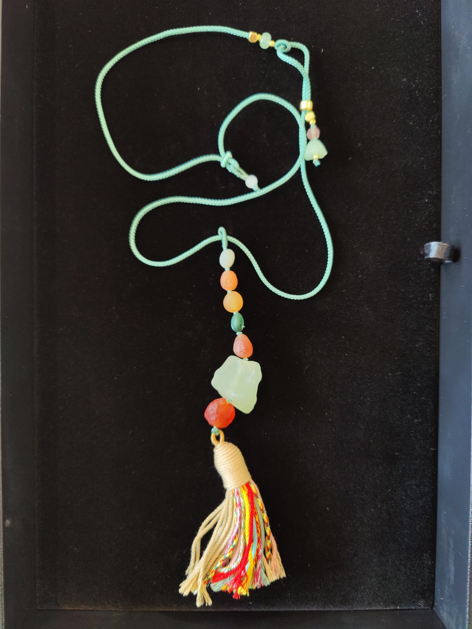 Gobi Desert Green Moss Agate pendant necklace with green and orange agate beads on an adjustable black cord laid on a textured surface