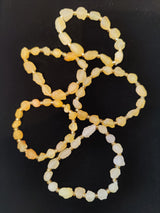 Four translucent agate beaded bracelets in varying soft yellow and cream tones arranged overlapping on a black background.