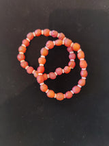Two elastic bracelets made of round, faceted orange-red beads with small white spacer beads, arranged overlapping on a black background.