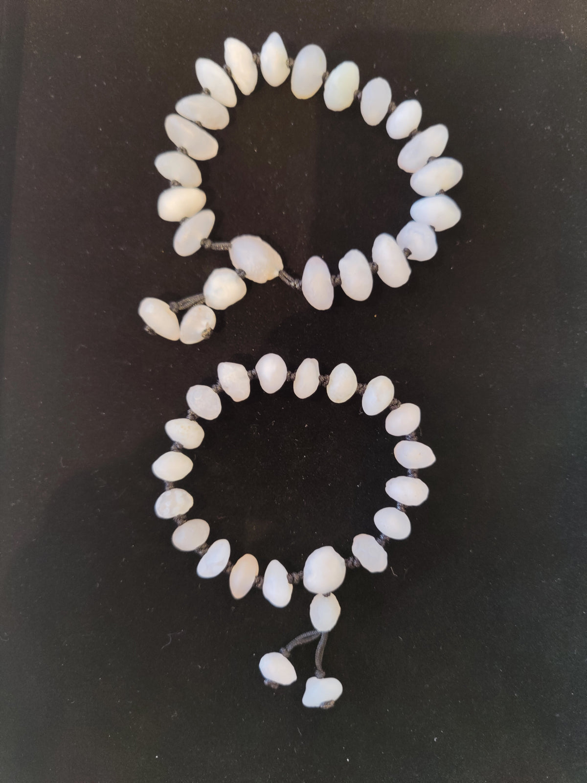 Two bracelets of white Gobi Desert agate beads, one larger with an extended bead cluster, both on a dark surface.