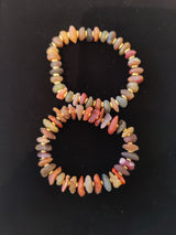 Two beaded bracelets made of irregular, smooth Gobi Desert agate stones in earthy tones of red, orange, gray, and beige, displayed on a black background.