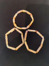 Three hand-strung bracelets made of small, irregularly shaped beads in cream, beige, and muted pastel shades against a black background.