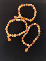 Three beaded bracelets with round, matte beads in varying warm tones including yellow, orange, red, and purple set against a black background.