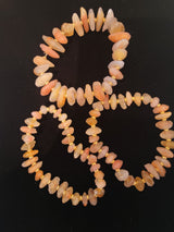 Three elastic bracelets composed of irregular peach and pink Gobi Desert agate beads with small gold spacer beads, arranged on a black background.