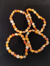 Three strands of small, rounded Gobi Desert Agate beads in soft orange, yellow, white, and red hues on a black background.