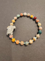 Multicolored jasper bead bracelet with a light gray turtle-shaped charm and small turquoise spacer beads on a dark gray background.