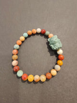 Beaded bracelet with round jasper stones in various earthy colors and a light blue-green cat-shaped animal charm, set against a gray background.