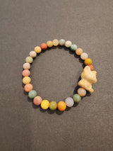 Beaded bracelet with round multi-color jasper beads and a small carved cream-colored animal charm, displayed on a dark background.