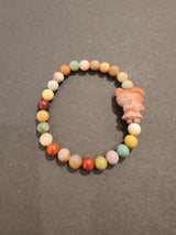Round multi-colored jasper bead bracelet with a small carved animal charm in soft pink attached on a dark gray background.
