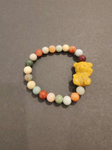 Round bead bracelet featuring multicolored jasper beads with a small carved yellow animal-shaped charm on a dark gray background.