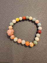 Jasper multi-color bead bracelet featuring round pastel and earth-toned beads with a carved animal-shaped charm on a dark gray background.
