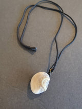 Light beige Gobi Desert Eye agate pendant with natural circular pattern, hanging from a simple black cord necklace against a plain dark gray surface.