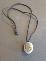 Oval pendant with green and cream cellular pattern on a black cord necklace against a gray background.