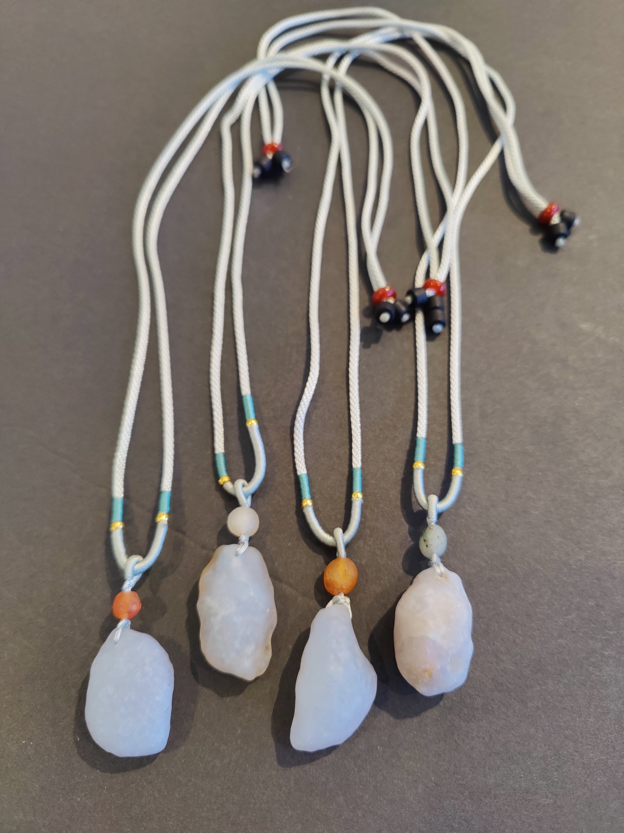 Raw Blue Chalcedony stone pendant hanging on an adjustable gray drawstring cord necklace against neutral background