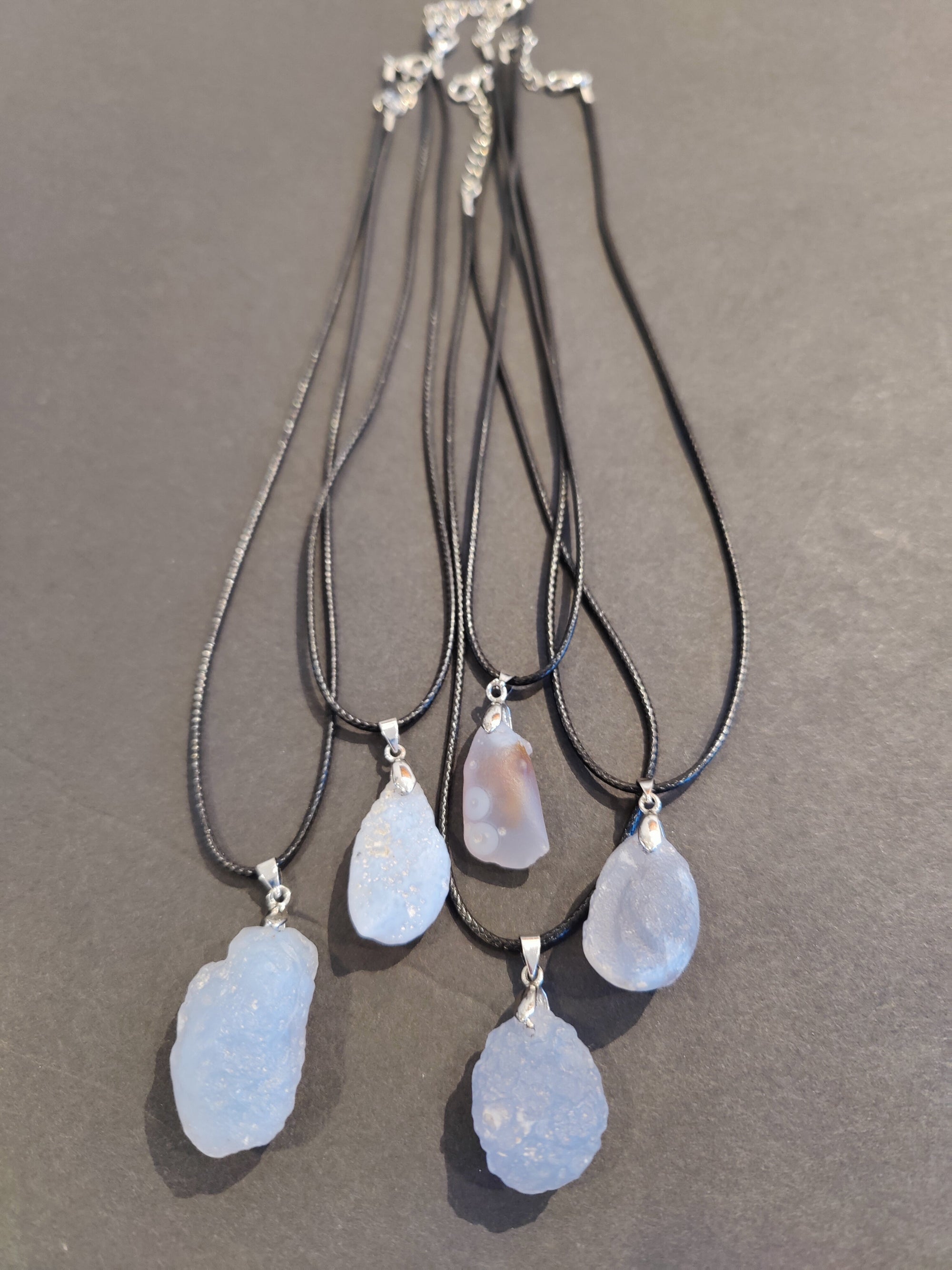 Close-up of Blue Chalcedony raw stone pendant hanging on a black cord necklace with stainless steel clasp
