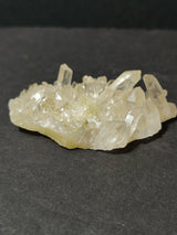 Cluster of transparent to milky white quartz crystal points with sharp facets, resting on a pale beige base against a dark background.