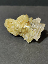 Yellowish and clear Quartz point crystal cluster with multiple pointed terminations, displayed on a dark surface, showing translucent and reflective surfaces.