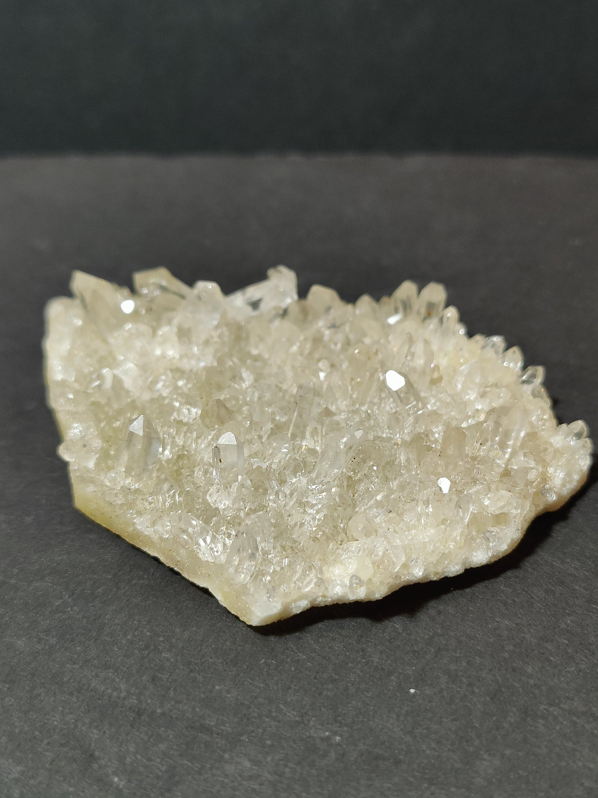 Irregular cluster of translucent white quartz points with small, sharply defined crystals on a dark surface.