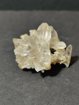 Cluster of translucent quartz points with sharp terminations and a slightly milky appearance, resting on a dark grey surface.