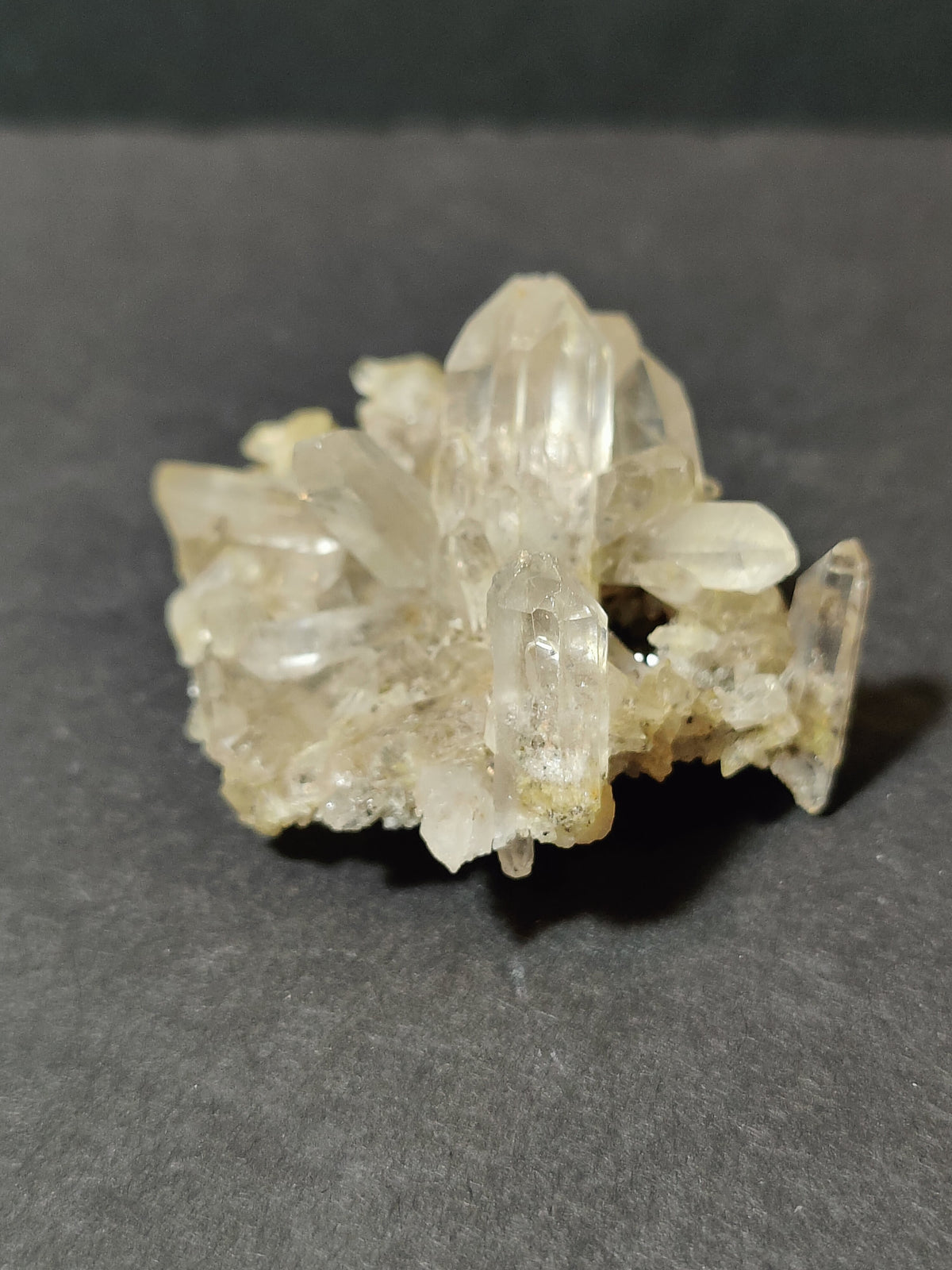 Cluster of translucent quartz points with sharp terminations and a slightly milky appearance, resting on a dark grey surface.