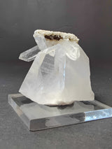 Clear quartz crystal cluster with a smaller elongated point protruding from a larger translucent base, topped by small white mineral formations, displayed on a clear square stand.