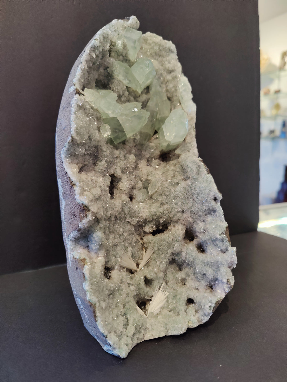 Vertical apophyllite cabinet specimen with pale green translucent crystals emerging from a white, crystalline geode base on a dark background.