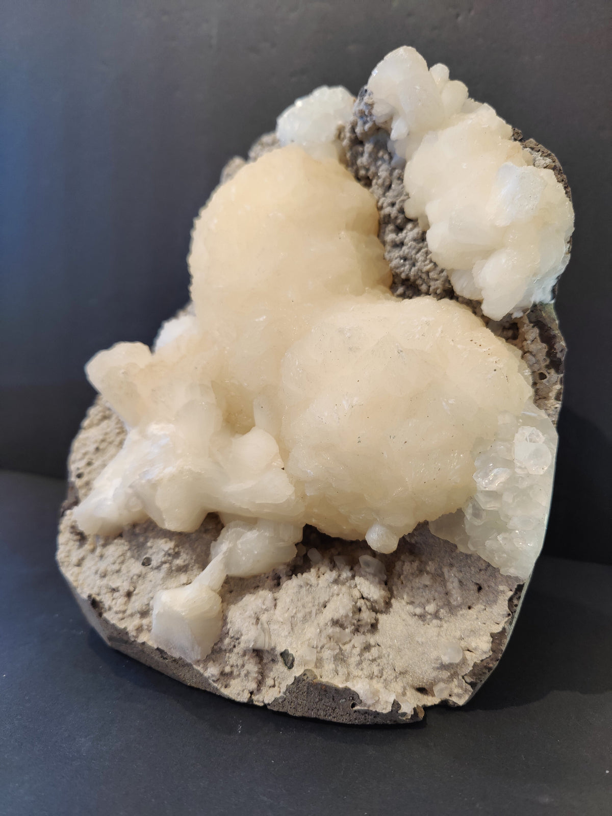 Creamy white stilbite crystals forming rounded clusters with translucent clear apophyllite on a rough, grayish matrix base against a black background.