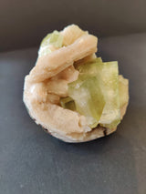 Cluster of pale green apophyllite cubes intergrown with elongated peach stilbite crystals on a dark background, showcasing contrasting crystal shapes and soft colors.