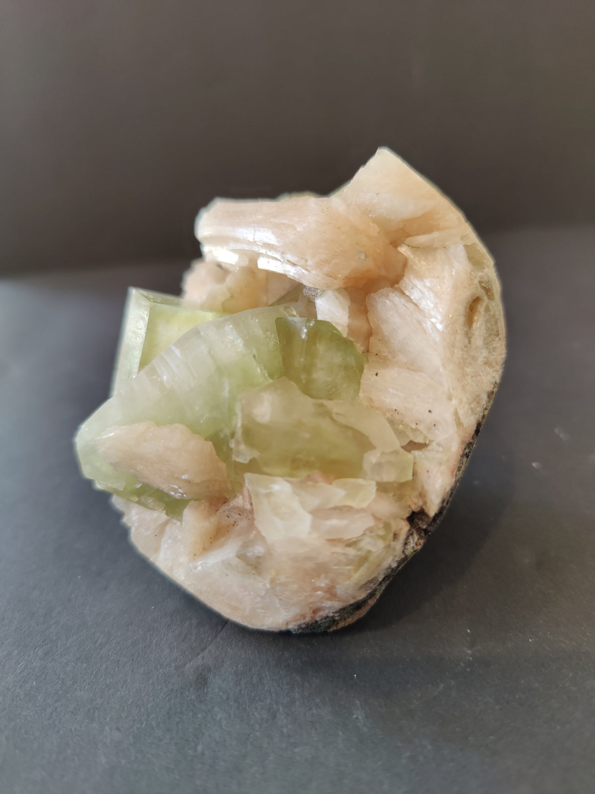 Cluster of translucent green apophyllite cube crystals alongside pale peach stilbite formations on a rough matrix base, viewed frontally against a dark background.