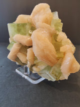 Cluster of translucent green apophyllite cubes intergrown with smooth, peach-colored stilbite formations, displayed on a clear stand against a dark background.