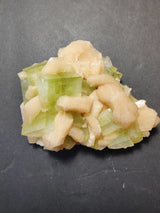 Green apophyllite crystals interspersed with creamy peach-colored stilbite formations, arranged in a rough cluster on a dark background.