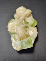 Cluster of pale peach stilbite crystals intertwined with translucent green apophyllite cubes on a dark background.