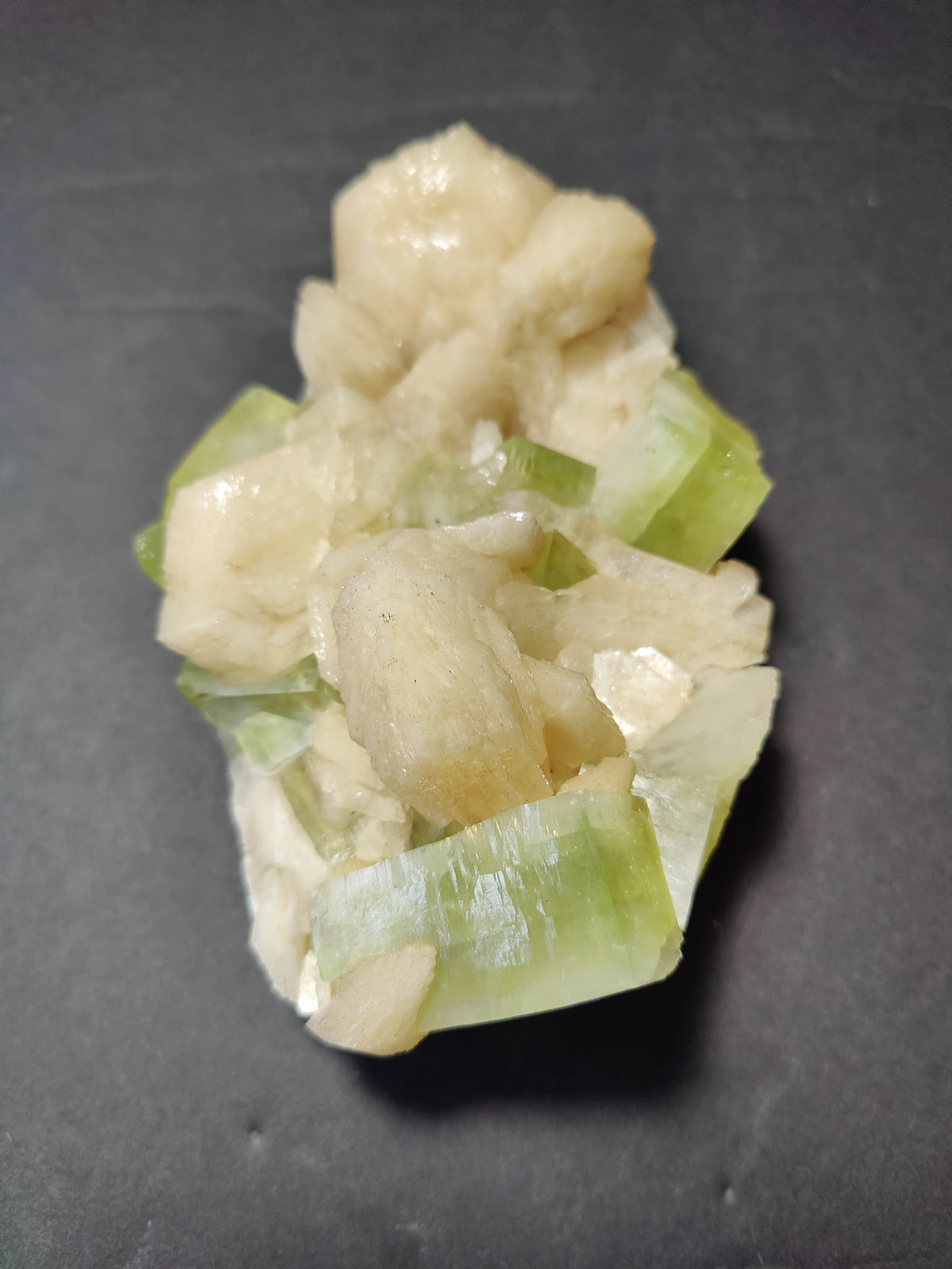 Cluster of pale peach stilbite crystals intertwined with translucent green apophyllite cubes on a dark background.