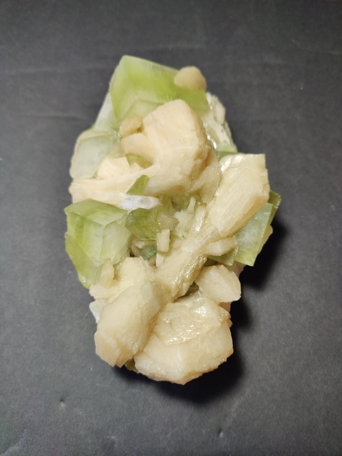 Cluster of translucent green Apophyllite cubes intergrown with creamy peach Stilbite crystals on a dark background, highlighting their contrasting shapes and colors.