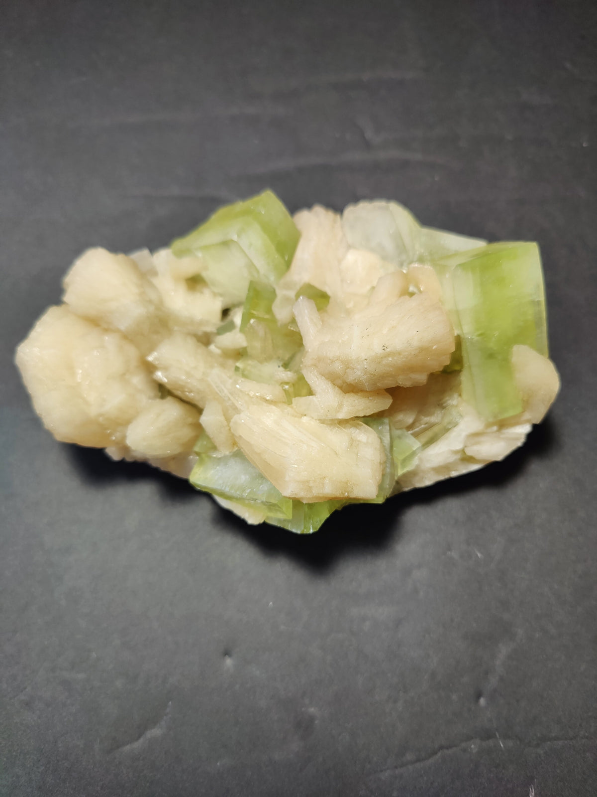 Cluster of green translucent apophyllite cubes intergrown with peach-colored stilbite crystals on a dark gray background