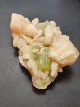 Cluster of pale peach stilbite crystals surrounding translucent green apophyllite cubes on a dark gray background.