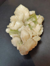 Cluster of pale peach stilbite crystals interspersed with translucent green apophyllite cubes on a dark surface, showing natural crystal shapes and glossy textures.