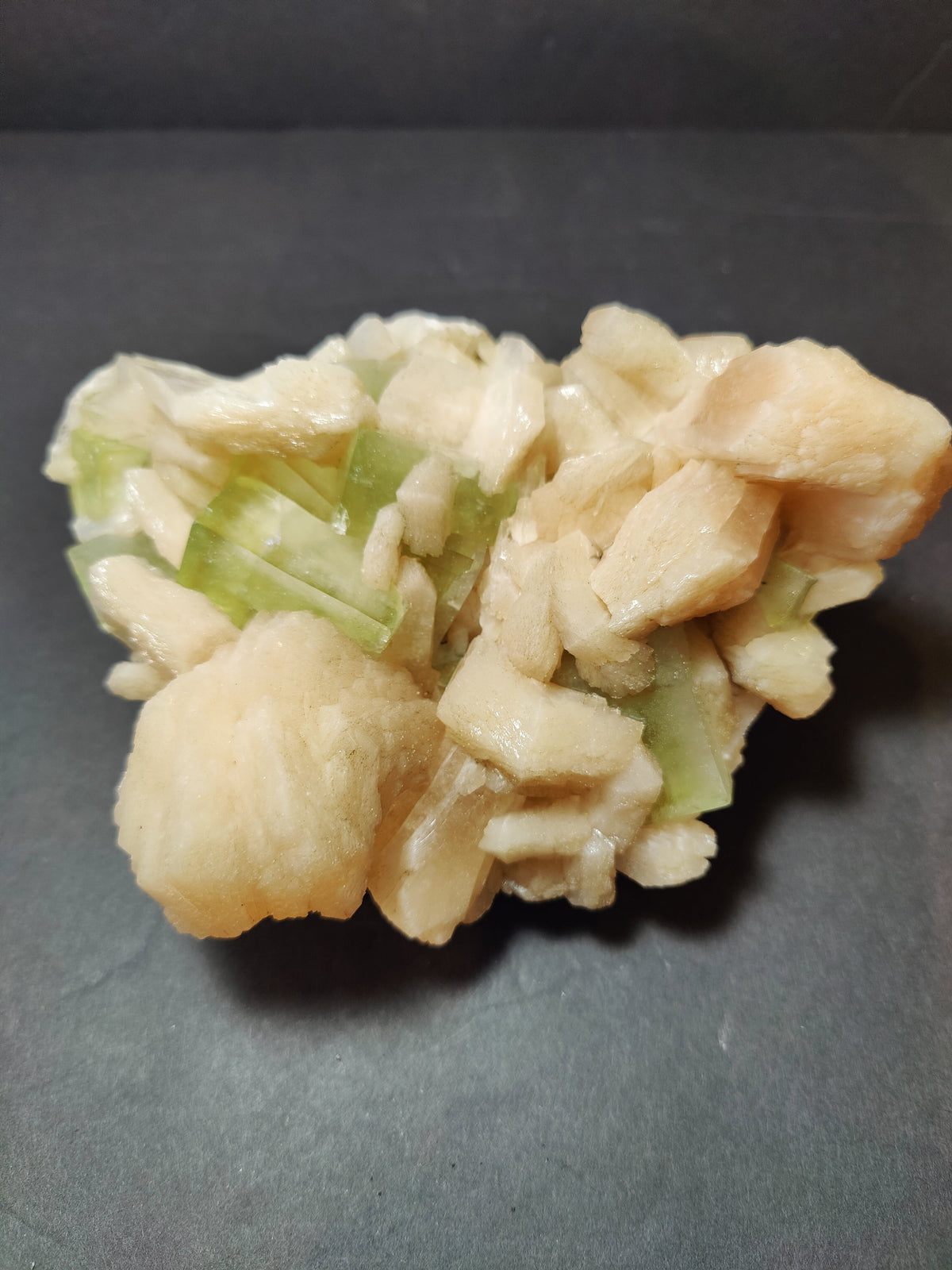 Cluster of pale peach stilbite crystals interspersed with translucent green apophyllite cubes on dark background.