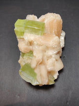Cluster of translucent green apophyllite cubes interspersed with peach-colored stilbite formations on a dark background.