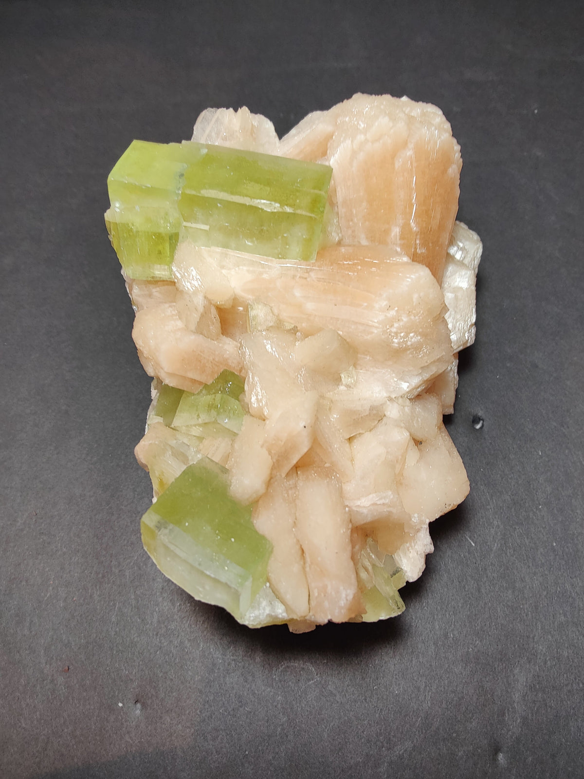 Cluster of translucent green apophyllite cubes interspersed with peach-colored stilbite formations on a dark background.
