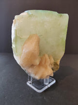 Green translucent apophyllite cube with attached peach-colored stilbite crystals on a clear plastic stand against a dark background.
