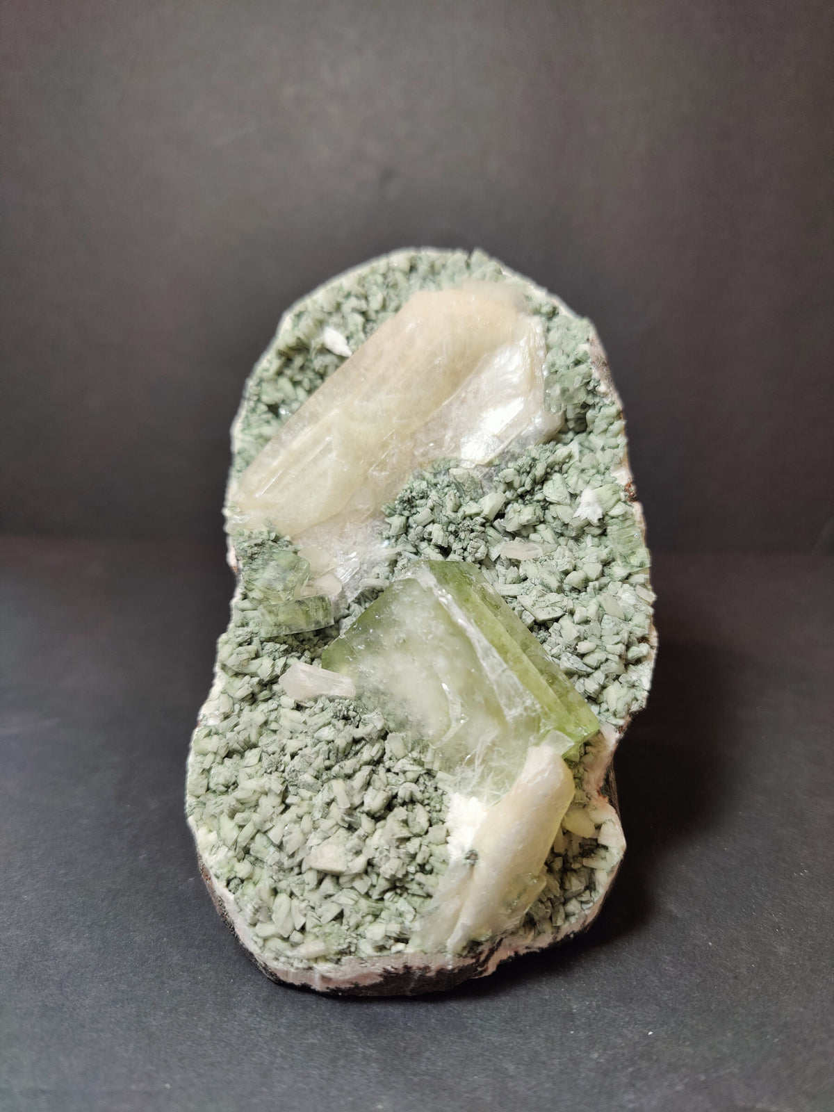 Heulandite specimen featuring pale green apophyllite cubes and peach stilbite crystals set in textured green matrix against a dark background.