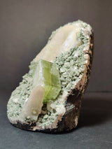 Green translucent apophyllite cube with smaller peach stilbite crystals on a pale green heulandite matrix, displayed against a dark background.