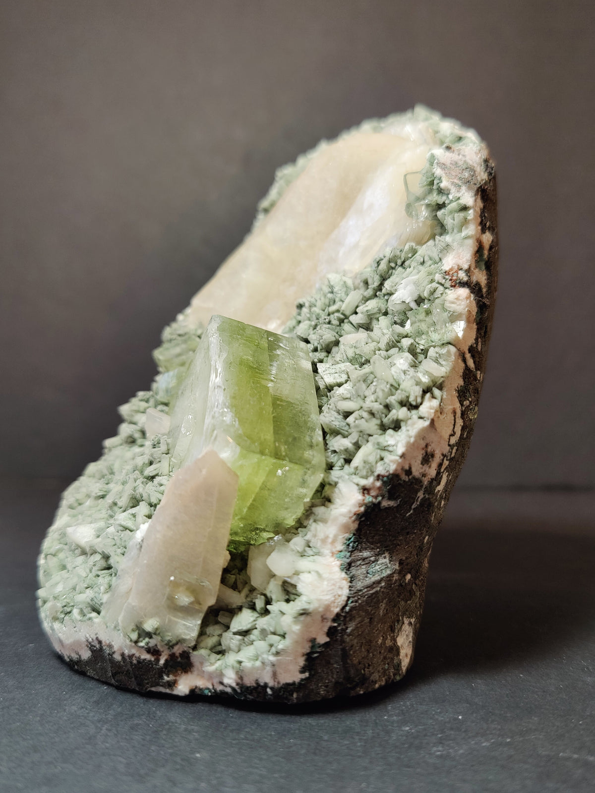 Green translucent apophyllite cube with smaller peach stilbite crystals on a pale green heulandite matrix, displayed against a dark background.